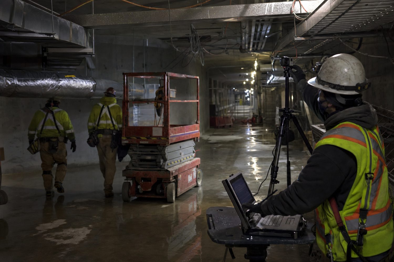Technicians calibrating a camera view in a dark interior work zone under temporary lighting