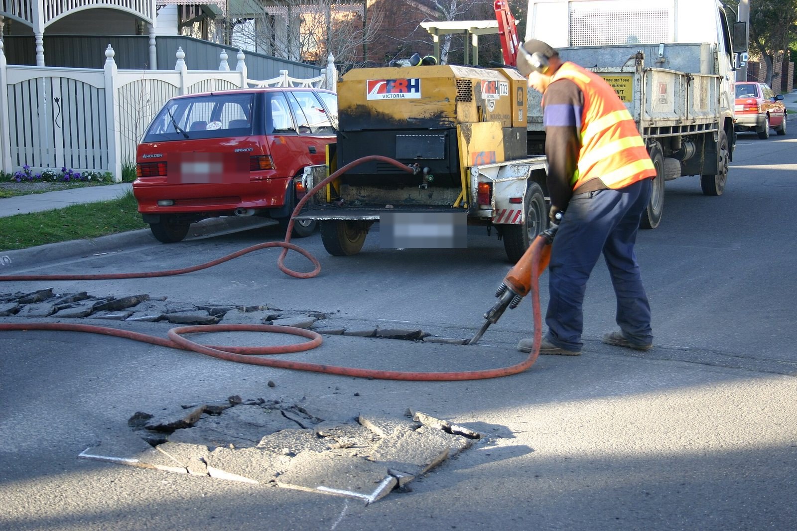 Worker in hearing protection breaking pavement with a jackhammer